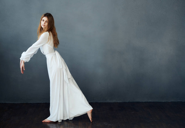 Mulher bonita em um vestido branco para o chão em um fundo cinza em pleno crescimento - Foto, Imagem