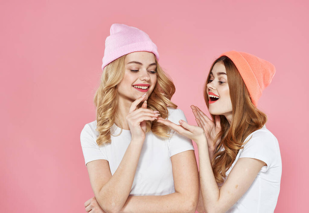 two girlfriends in multicolored caps hugs glamor pink background - Foto, Imagen