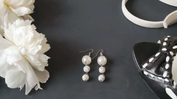 ramo de peonía blanca, pendientes con perlas, bolso de mujer y zapatos sobre fondo negro, primer plano - Metraje, vídeo