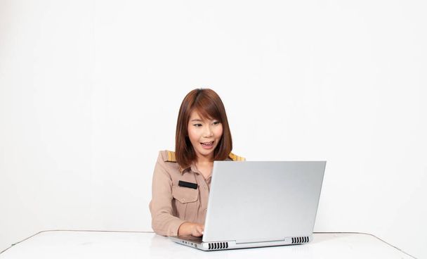 Female thai teacher in uniform sitting with white background using computer and smiling - Photo, Image