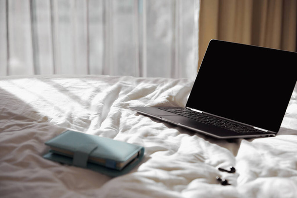 Laptop, planner and headphones on bed in sunlight - Photo, Image