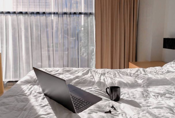 Laptop, planejador e fones de ouvido na cama à luz do sol - Foto, Imagem
