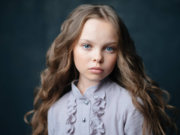 Πορτρέτο ενός όμορφου κοριτσιού με σγουρά μαλλιά και γκρι φόρεμα σε σκούρο φόντο - Φωτογραφία, εικόνα