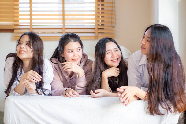 Grupo de cuatro mujeres asiáticas tumbadas en la cama sonrisa mira la cámara se siente feliz amigos o adolescentes que se divierten en la acogedora habitación en casa - Foto, imagen