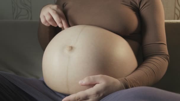 pregnant woman sitting on couch, playing with belly, stepping on it with fingers - Filmati, video