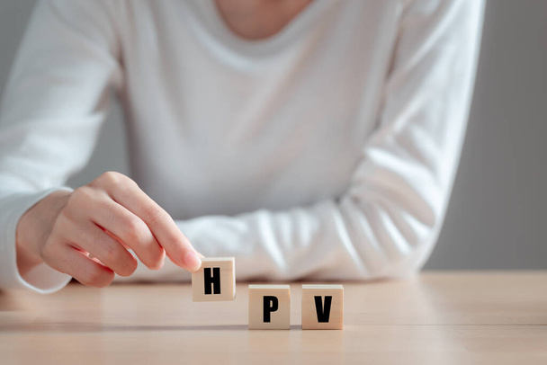 HPV (Human Papillomavirus) akronim na bloku drewna, Azjatka trzymająca drewniany blok, wirusy Niektóre szczepy infekują genitalia i mogą powodować raka szyjki macicy. Koncepcja zdrowia kobiet. - Zdjęcie, obraz
