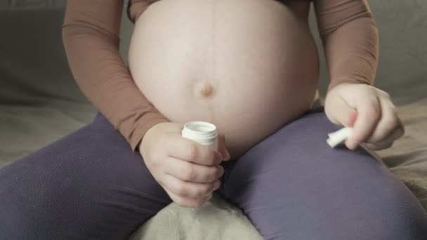 pregnant woman sitting on couch, opening bottle of pills, showing medicine - Video, Çekim