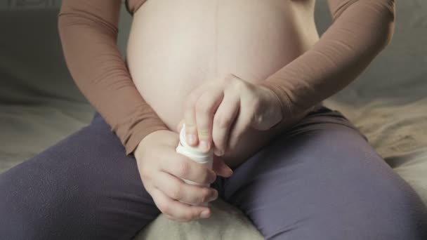 pregnant woman sitting on couch, opening bottle of pills, showing medicine - Imágenes, Vídeo