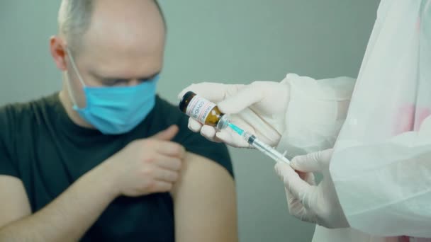 Equipo médico de vacunación con jeringa con aguja y ampolla en la mano del médico o enfermero sobre el fondo del paciente masculino del grupo de riesgo en el hospital - Metraje, vídeo