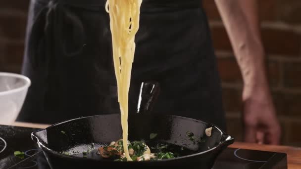 Chef puts spaghetti pasta in a frying pan with fried mushrooms, garlic and parsley in a restaurant kitchen. Food ingredient. . Prepare food to eat. Italian culinary. Delicious dinner - Footage, Video