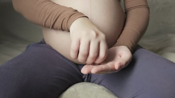 pregnant woman sitting on couch, pouring out fish oil from bottle on her palm - Záběry, video