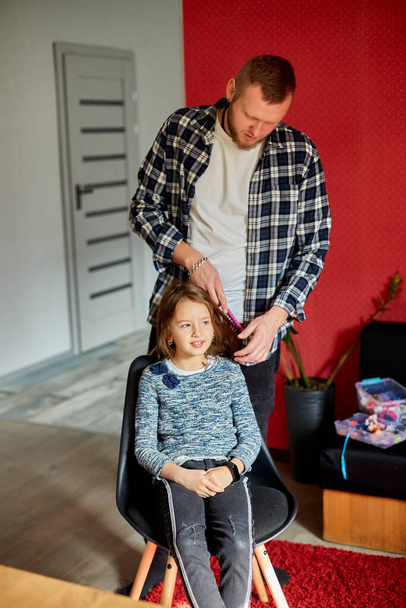 Padre peinando, cepillando el pelo de su hija en casa, padre e hija sonriendo, momentos familiares, pasando tiempo juntos. - Foto, imagen