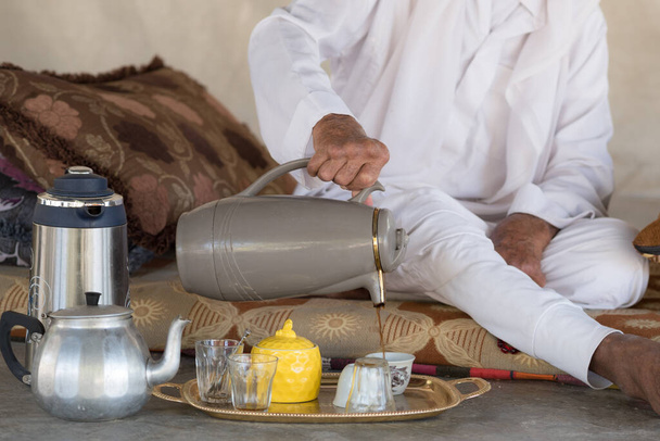 Arab Bedouin Man se sienta en el suelo y sirve té o café de - Foto, imagen