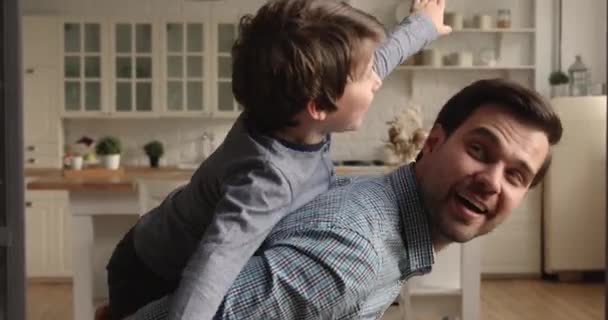 Happy dad piggybacks little preschool son playing together at home - Filmati, video