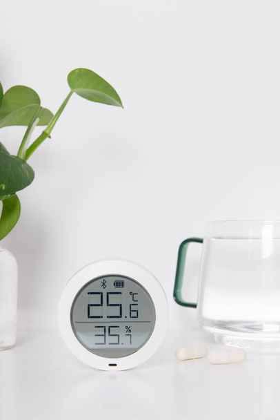 Hygrometer, Kopfschmerztabletten und ein Glas Wasser auf weißem Hintergrund. Das Mikroklima im Haus. - Foto, Bild