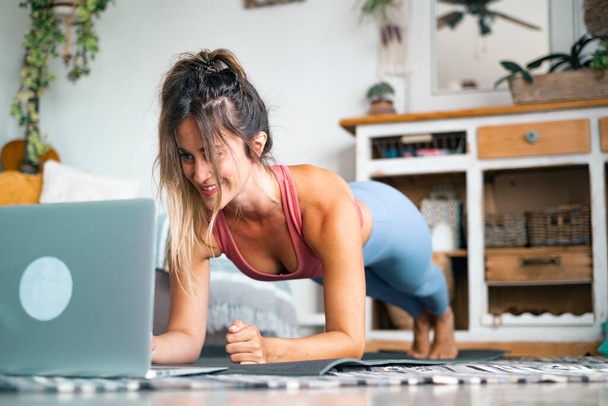 Nuori nainen käyttää kotona tekemällä push ups ja katsomalla hänen henkilökohtainen kannettava tietokone oppia tai opettaa harjoitus - Valokuva, kuva