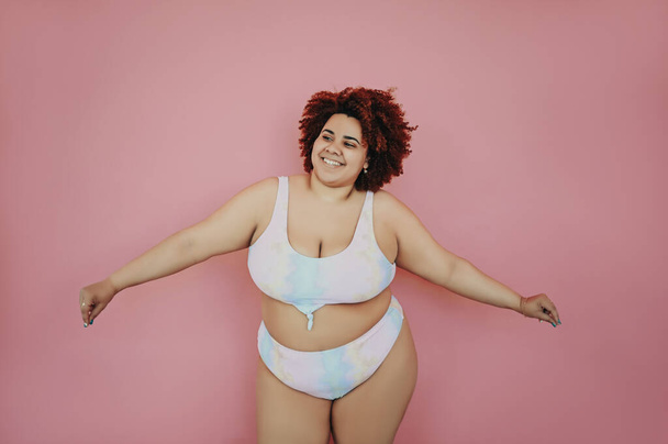 Glücklich lächelnd emotionale kurvige übergroße afrikanische schwarze Frau Afrohaar posiert in Badeanzug rosa Hintergrund isoliert, Körper Unvollkommenheit, Körperakzeptanz, Körper positive und Diversity-Konzept. Kopierraum. - Foto, Bild