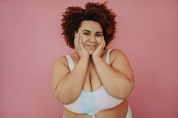 Happy smiling emotional curvy oversize African black woman afro hair posing in swimsuit pink background isolated, body imperfection, body acceptance, body positive and diversity concept. Copy space. - Photo, Image
