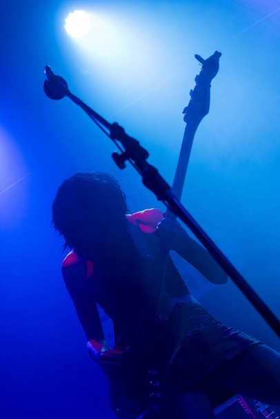 Nerozpoznatelný ženský kytarista s krátkými vlasy. Hudební světla ukazují siluetu během koncertu rockové kapely. Mlhavé světlo - Fotografie, Obrázek
