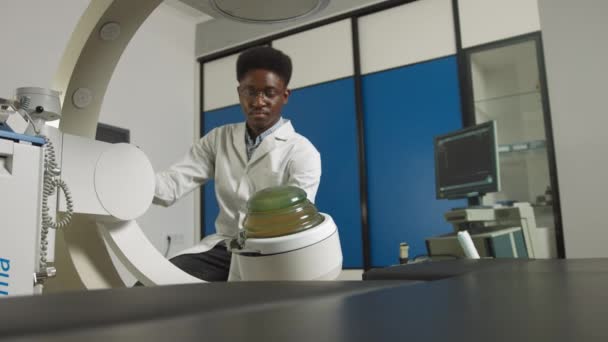 Dolní pohled na mladého sebevědomého afrického lékaře v bílé uniformě, který pracuje s moderním litotrypařským vybavením pro léčbu ledvinových kamenů. Neinvazivní extrakorporální rázová vlna litotrypse - Záběry, video