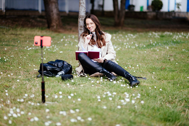 улыбающаяся студентка дистанционно учится на открытом воздухе в парке - Фото, изображение