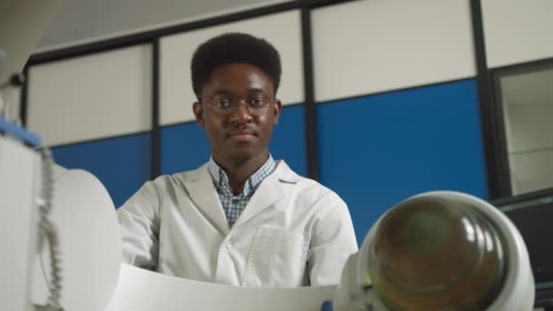 Dolní pohled na mladého sebevědomého afrického lékaře v bílé uniformě, který pracuje s moderním litotrypařským vybavením pro léčbu ledvinových kamenů. Neinvazivní extrakorporální rázová vlna litotrypse - Záběry, video