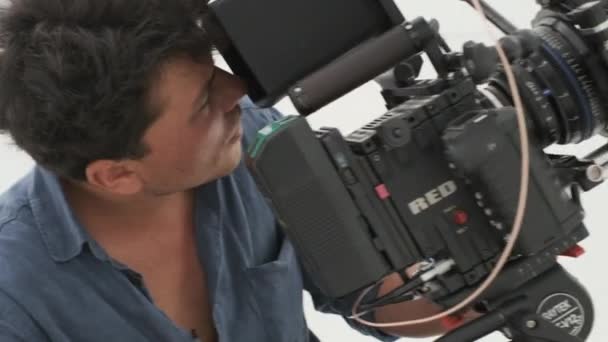 Kameramies farkkupaidassa kuvaa punaisella kameralla. Clouse-up valkoisella pohjalla - Materiaali, video