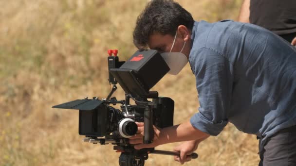 Kameramann im Jeanshemd schießt auf rote Kamera in der Natur. Clouse-up auf verschwommenem Hintergrund - Filmmaterial, Video