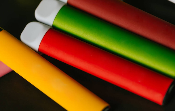 Värikkäitä kertakäyttöisiä sähkösavukkeita mustalla taustalla. Tupakoinnin, höyryn ja nikotiinin käsite - Valokuva, kuva