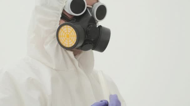 Detailní záběr muže v bílém ochranném obleku a plynové masce drží bílou plastovou trubici, ze které vychází kouř - Záběry, video