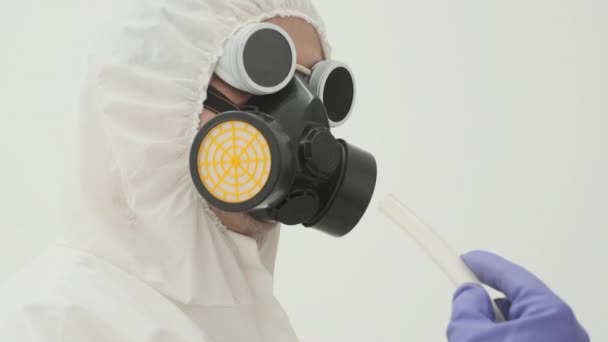 Gros plan de l'homme en combinaison de protection chimique blanche et masque à gaz tenant un tube en plastique blanc d'où sort la fumée - Séquence, vidéo