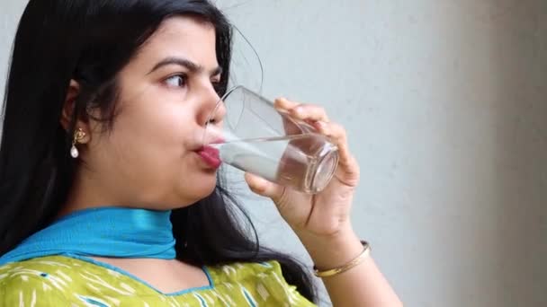 Vista lateral de una hermosa mujer india bebiendo agua de vidrio sobre fondo blanco - Imágenes, Vídeo
