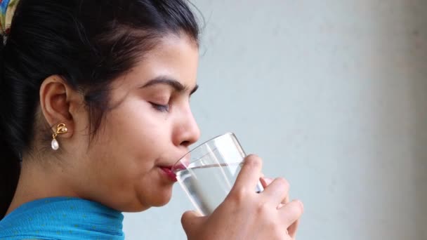 Vue latérale rapprochée d'une jolie Indienne buvant de l'eau du verre sur fond blanc - Séquence, vidéo
