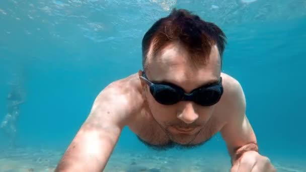 Mies ui suojalaseissa veden alla ja piteli kameraa, Egeanmeren rannalla. Hidasta vauhtia, vedenalainen ammunta. Kreikka - Materiaali, video