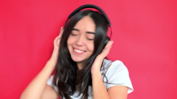 Το κορίτσι ακούει μουσική με ακουστικά. Χαμογελάει. Κόκκινο φόντο - Πλάνα, βίντεο