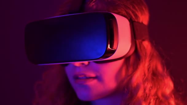 Νεαρό κορίτσι μαλλιά τζίντζερ χρησιμοποιώντας ακουστικά εικονικής πραγματικότητας με πολύχρωμα φώτα νέον - Πλάνα, βίντεο