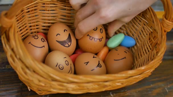 Stack of hand drawn smiley eggs on straw basket with colorful candy, easter preparation, holiday mood concepts - Footage, Video