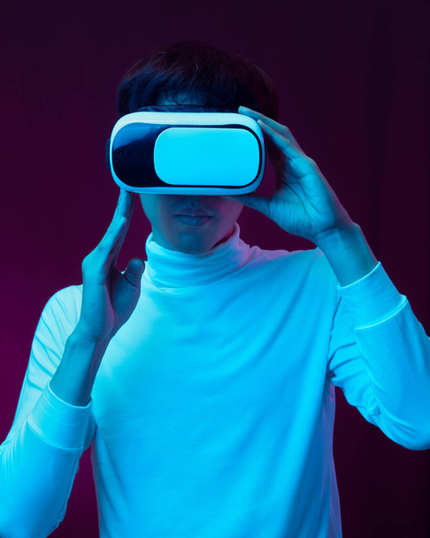 Jeune homme asiatique portant des lunettes de réalité virtuelle regardant la vidéo à 360 degrés dans la lumière au néon, concept de technologie. - Photo, image