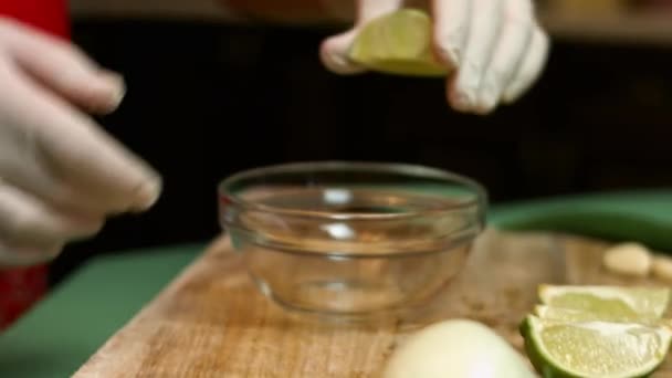 A női kéz friss lime-ot présel. A citromlé beleesik egy üvegtálba. Salsa készítés folyamata. Művészeti fotózás - Felvétel, videó