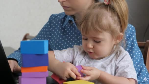 A freelance woman works at home at a computer with a small child in her arms, mother and child spend time together, the child plays with cubes, the life of an adult is online in social networks - Footage, Video