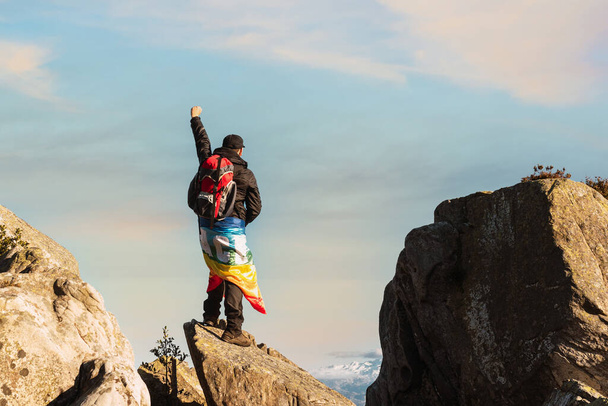 escursionista in piedi su una roccia nella montagna, alzando il pugno e portando una bandiera arcobaleno di pace. sport e inclusione. combattere per la pace. alpinista contemplando le montagne. - Foto, immagini