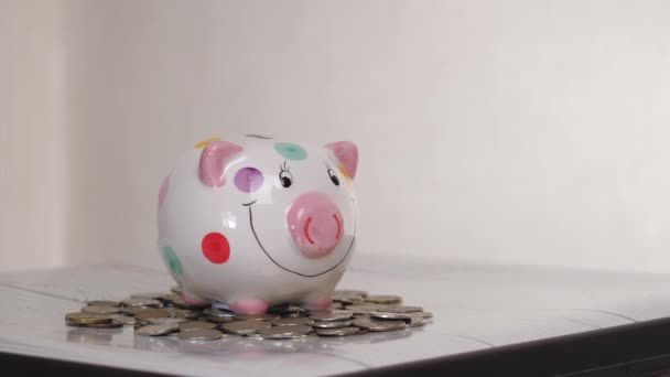 Das Sparschweingeschäft steht auf einem Haufen Münzen. Eine Hand steckt eine Münze in ein Lifestyle-Sparschwein auf gelbem Hintergrund. Geld zu sparen ist eine Investition in die Zukunft. Bankeninvestitionen. - Filmmaterial, Video
