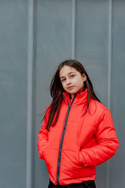 фото девочки-подростка на сером фоне стены. Подросток в оранжевой куртке. портрет, - Фото, изображение