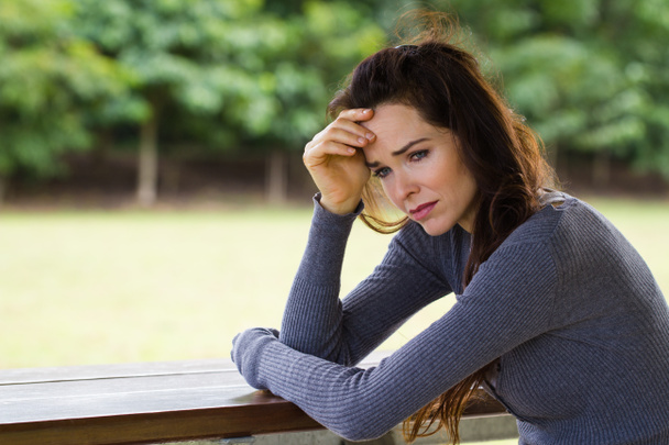 Sad and worried woman sitting outdoors - Фото, изображение