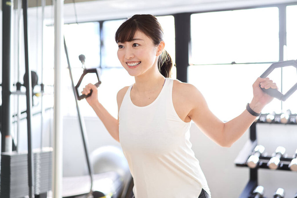 Asian woman using a cable machine in a training gym - Photo, image