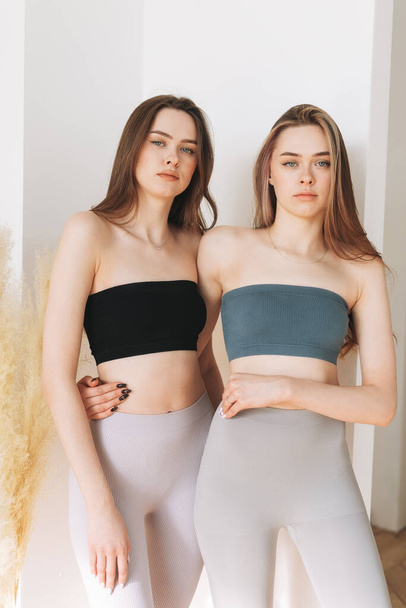 Мода модели красоты две сестры близнецы красивые девушки с длинными волосами в спортивной одежде глядя на камеру в яркой студии - Фото, изображение