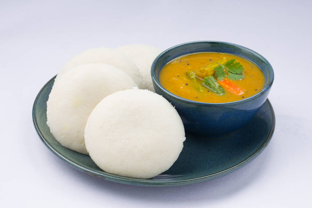 Idly ή Idli, νότια ινδική κύριο στοιχείο πρωινό το οποίο είναι όμορφα τοποθετημένα σε πιάτα aaqua χρώμα με ένα μικρό μπολ sambar τοποθετείται σε λευκό φόντο. - Φωτογραφία, εικόνα