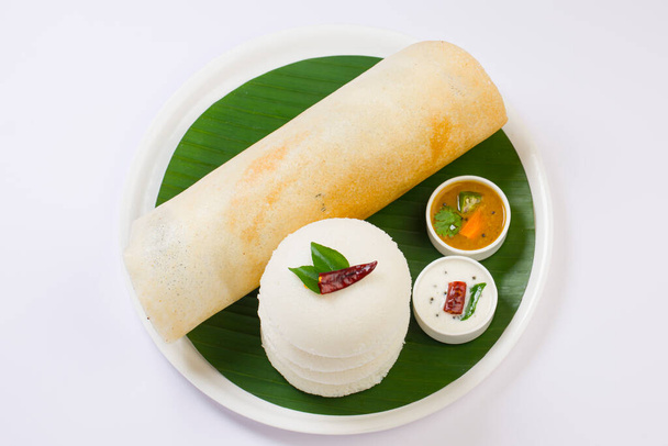 Ghee roast Dosa e Idlii, plato principal de desayuno del sur de la India que está bellamente dispuesto en un plato blanco forrado con hoja de plátano y curry como sambar y chutney sobre fondo blanco. - Foto, imagen