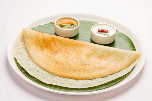 Ghee arrosto Dosa, sud indiano elemento principale colazione che è ben organizzato come una faccia sorriso in un piatto bianco foderato con foglia di banana su sfondo bianco. - Foto, immagini