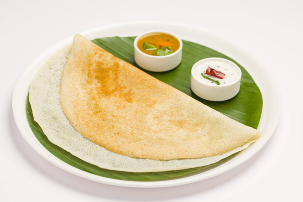 Ghee gebraden Dosa, Zuid-Indiase belangrijkste ontbijt item dat prachtig is ingericht als een glimlach gezicht in een witte plaat bekleed met bananenblad op witte achtergrond. - Foto, afbeelding